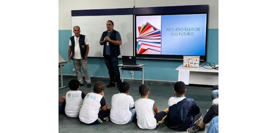 A imagem mostra uma apresentação do projeto "Eleitor do Futuro" em um auditório escolar. Um home...