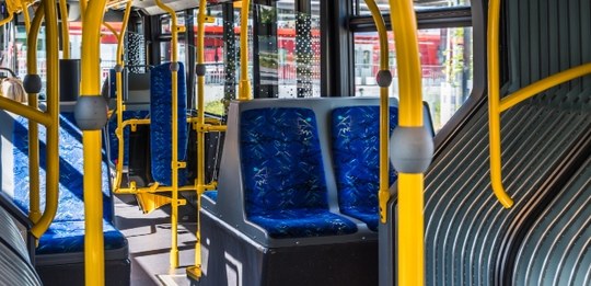Fotografia do interior de um ônibus urbano iluminado pela luz do sol. Em destaque, assentos dupl...