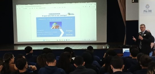 Turma de estudantes sentados em cadeiras verdes, assistindo a uma palestra conduzida por juíza. ...