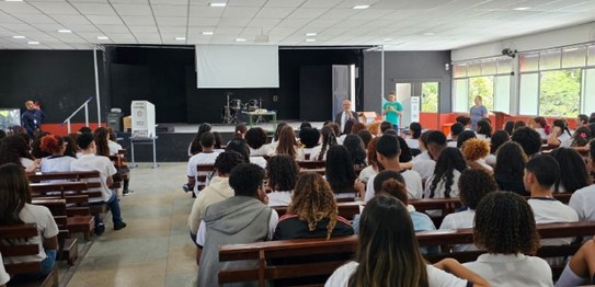 Turma de estudantes sentados em cadeiras verdes, assistindo a uma palestra conduzida por juíza. ...