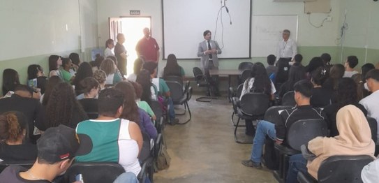 Turma de estudantes sentados em cadeiras verdes, assistindo a uma palestra conduzida por juíza. ...