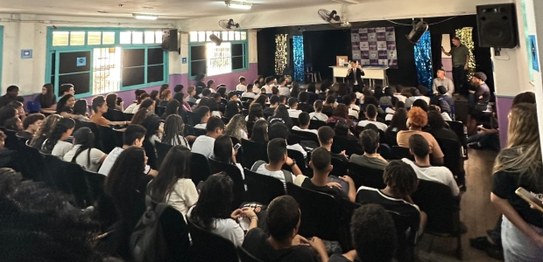 Turma de estudantes sentados em cadeiras verdes, assistindo a uma palestra conduzida por juíza. ...