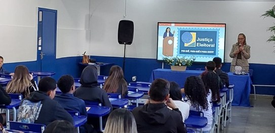Turma de estudantes sentados em cadeiras verdes, assistindo a uma palestra conduzida por juíza. ...