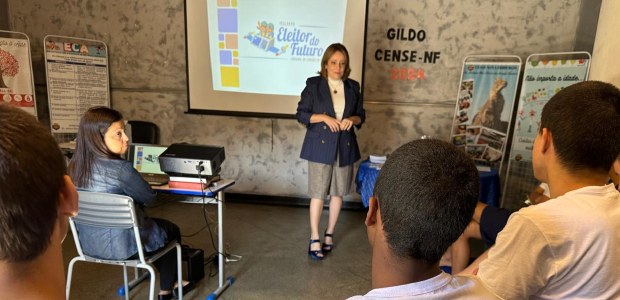 Mais de 1.200 estudantes participam das atividades do "TRE vai à escola" no mês de abril A juíza eleitoral está de pé e conversa com um grupo de jovens. Ao fundo, uma tela exibe um slid...