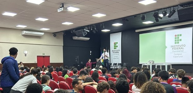 Auditório do Instituto Federal Fluminense (IFF) com diversos alunos sentados em poltronas vermel...