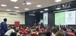 Auditório do Instituto Federal Fluminense (IFF) com diversos alunos sentados em poltronas vermel...