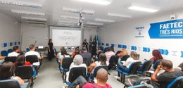 A imagem mostra uma sala de aula da Faetec Três Rios, com várias pessoas sentadas em cadeiras es...
