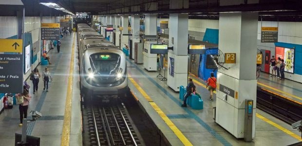 A imagem mostra a plataforma de uma estação do Metrô Rio com um trem se aproximando. A estação é...