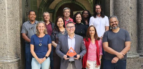 Michel Kovacs posa com troféu, em formato piramidal, ao lado de dez integrantes da equipe da TI,...