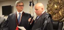 Rafael Estrela, homem branco e careca, vestindo toga, segura o microfone, lendo o documento de p...