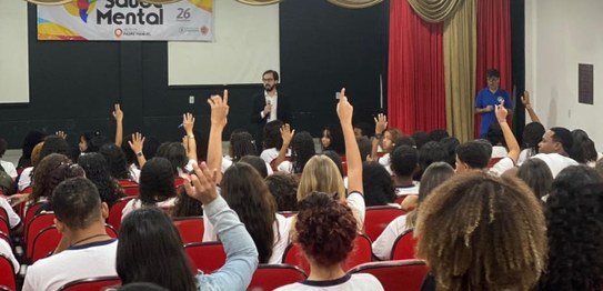 Numa sala, sentados, estudantes assistem à palestra da juíza eleitoral. Ela está de pé na frente...