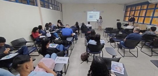 Numa sala de aula, sentados, estudantes assistem à palestra da juíza eleitoral Anna Carolinne Li...