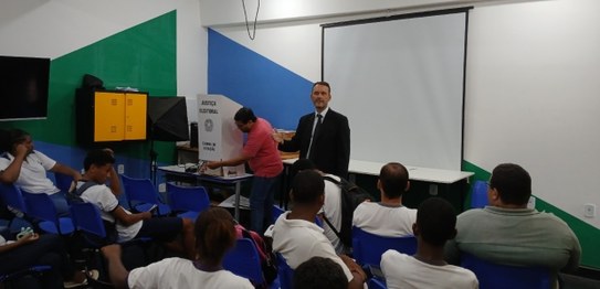 Palestrante realiza apresentação em sala com estudantes e responsáveis, com apoio de materiais i...