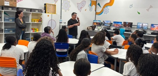 Em uma sala de aula decorada com desenhos nas paredes, um palestrante fala para estudantes senta...