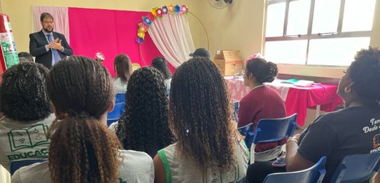 A imagem mostra um ambiente de sala de aula com um quadro branco ao fundo e estudantes sentados....