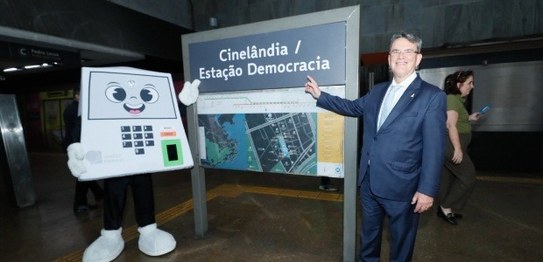 Na estação de metrô, o presidente do TRE-RJ Claudio de Mello Tavares aponta sorrindo para a plac...