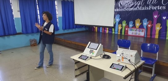 A imagem mostra uma apresentação do projeto "Eleitor do Futuro" em um auditório escolar. Um home...