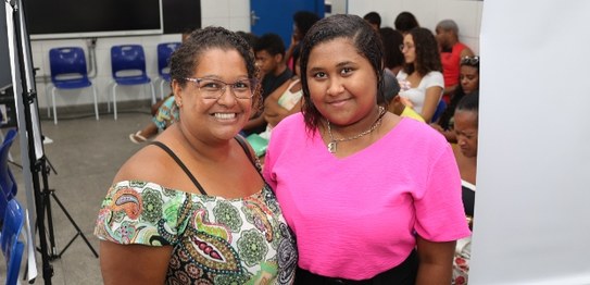 Duas eleitoras posam para foto, tendo ao fundo pessoas sentadas; às esquerda, mulher negra, com ...