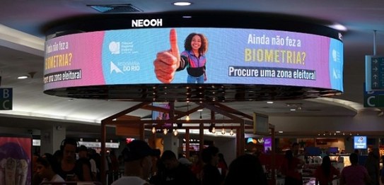 Praça do pedágio da Ecovias Ponte. Em cada guichê, há um painel digital exibindo um aviso sobre ...