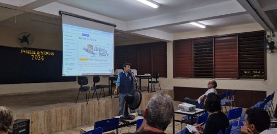 A imagem mostra uma apresentação do projeto "Eleitor do Futuro" em um auditório escolar. Um home...