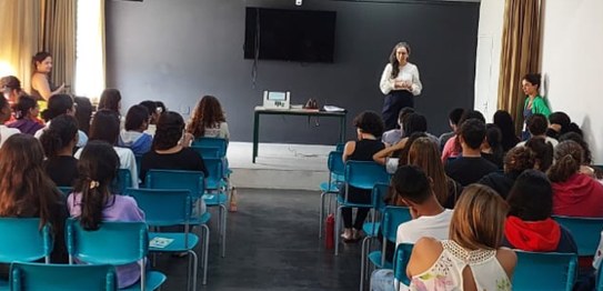 A imagem mostra uma apresentação do projeto "Eleitor do Futuro" em um auditório escolar. Um home...