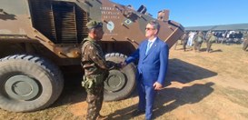 Em um campo aberto, ao lado de um veículo militar blindado nas cores verde e marrom, o president...