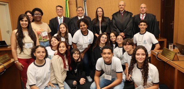 Primeiro voto e consciência cidadã: estudantes conhecem a Justiça Eleitoral fluminense por dentro Foto posada de um grupo de pessoas em um ambiente fechado. Os mais jovens estão abaixados, enqua...