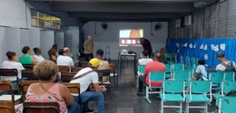 Descrição da imagem: Em pé, o servidor veste uma blusa verde e está de frente para os(as) alunos...