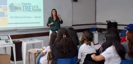 A imagem mostra uma sala de aula onde uma mulher está dando uma palestra para um grupo de estuda...
