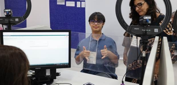 Projeto “Visitas ao TRE” recebe jovens do programa Sorrindo Inclusão Atendimento em posto da Justiça Eleitoral, onde um jovem com crachá faz gesto positivo diante de...