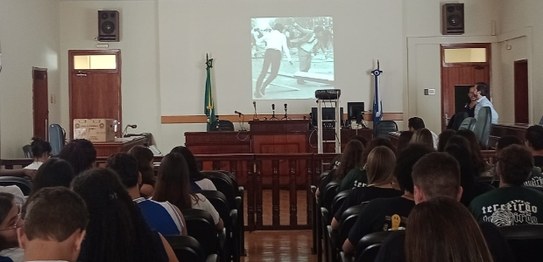 Descrição da imagem: À direita, o juiz Otávio Mauro Nobre, de camisa azul, projeta uma apresenta...