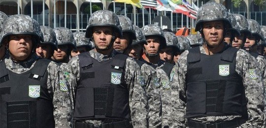 Foto mostra um grupo de militares uniformizados, usando capacetes e coletes de proteção, perfila...