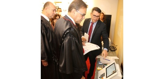 Secretário de TI apresenta novo modelo das urnas para membros e servidores do TRE-RJ Descrição da imagem: foto do hall do plenário do Tribunal, que tem paredes brancas e carpete ver...