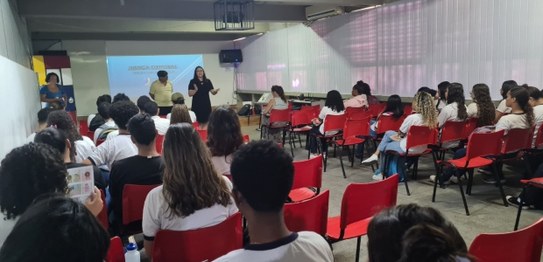 Numa sala, sentadas(os), estudantes assistem à palestra do juiz eleitoral Livingstone dos Santos...