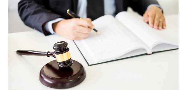 Em destaque, o martelo, que simboliza Justiça. Ao fundo, um homem de terno escreve em um livro