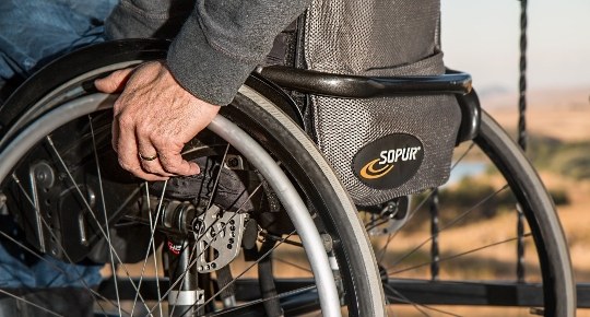 Imagem de uma cadeira de rodas com foco nas mãos que estão repousadas nas rodas