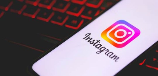 Celular exibindo o logotipo do Instagram sobre um teclado de computador, com iluminação em tons ...