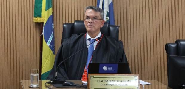 Foto do presidente do TRE-RJ, desembaragador Claudio de Mello Tavares, sentado à mesa, sobre o q...
