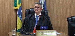 Foto do presidente do TRE-RJ, desembaragador Claudio de Mello Tavares, sentado à mesa, sobre o q...