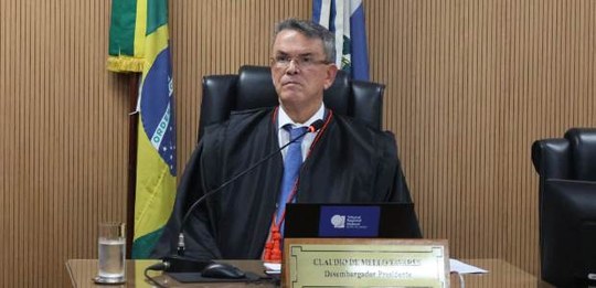 Foto do presidente do TRE-RJ, desembaragador Claudio de Mello Tavares, sentado à mesa, sobre o q...