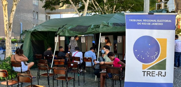 TRE-RJ atende mais de 400 eleitoras(es) no “Registre-se! 2025” Guichê de atendimento na ação Registre-se. Ao fundo uma tenda com os kits a frente, umas cadeira...