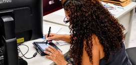 Mulher sentada diante de um computador utilizando uma mesa digitalizadora/caneta eletrônica para...