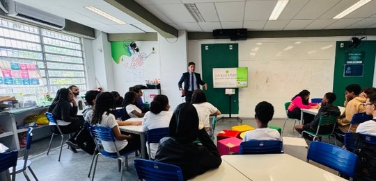 Um homem de terno conduz uma atividade sobre processo eleitoral para estudantes organizados em g...