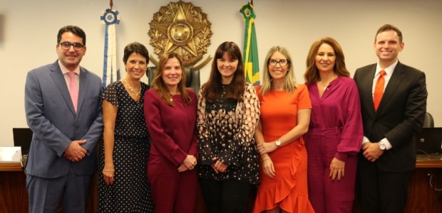 TRE-RJ discute avanços e retrocessos das mulheres nos espaços de poder Foto posada de participantes do evento, tendo ao fundo o brasão da República e bandeira do Brasi...