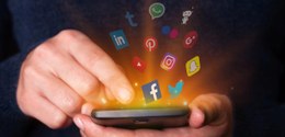 A imagem mostra uma pessoa segurando um smartphone, com diversos ícones de redes sociais "saindo...