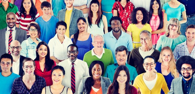 A imagem mostra um grupo de pessoas diversas em pé, próximas umas das outras.