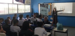 Em pé, na frente da sala de aula, a servidora Isabela Feijó aponta para o quadro branco, durante...