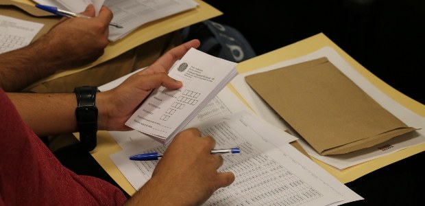 TRE-RJ estudantes da UVA preenchem cédulas que serão utilizadas no dia da votação Foto em detalhe, onde temos as mãos de um dos participantes do evento segurando algumas cédulas ...