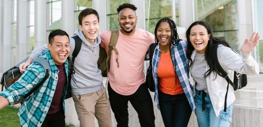 A imagem mostra cinco jovens posando juntos e abraçados, eles sorriem para a câmera e vestem rou...