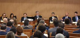 A imagem mostra uma sala cheia de pessoas sentadas em fileiras, sugerindo um ambiente formal de ...